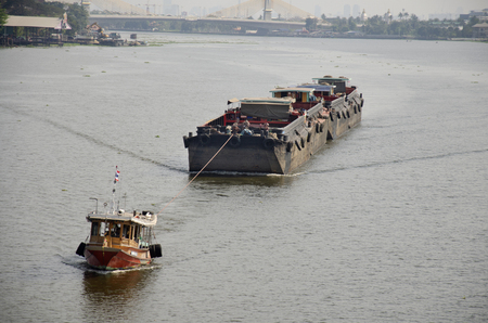 Asian thai people sailing barge and tugboat cargo ship in Chao Phraya or chaopraya river from Bangkok go to Ayutthaya at Phra Nang Klao bridge in Nonthaburi, Thailandの写真素材
