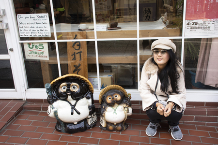 Tokyo, Japan - March 31, 2019 : Travelers thai women posing portrait for take photo with japanese raccoon dog or Tanuki in Naritasan Omote Sando or Narita old town at Chiba on March 31, 2019 in Tokyo, Japanのeditorial素材