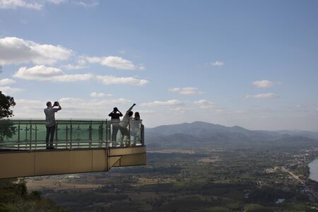 Travelers thai people travel visit and posing for take photo view of landscape of Nongkhai city and loas and Mekong river on glass skywalk of cliffs at Wat Pha Tak Suea temple in Nong Khai, Thailandの写真素材