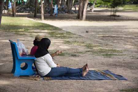 Thai couple lover people sit and dating on mat and stone bench on Samila Beach at Hat Yai city in Songkhla, Thailand の写真素材