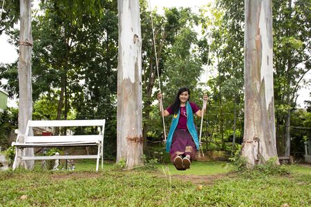 Thai woman sit relax and playing on wooden bench swings toy in garden of resort at riverside Mae...