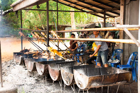 MUKDAHAN, THAILAND - NOVEMBER 12 : Thai chefs people cooking roast and grill barbecued suckling pig on charcoal stove in kitchen of restaurant at Kaengkabao on October 12, 2019 in Mukdahan, Thailandのeditorial素材