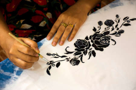 Thai woman people artist painting pattern with natural color indigo on fabric shawl scarf on table...