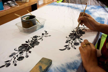 Thai woman people artist painting pattern with natural color indigo on fabric shawl scarf on table...