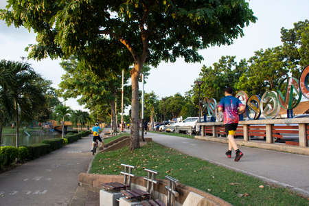 Asian thai people and foreign travelers walking jogging exercise  biking bicycle on pathway around pondside in dusk time at Nong Prajak public garden park on September 15, 2020 in Udon Thani, Thailandのeditorial素材