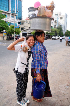 Travelers thai women travel visit buying food burma style and take photo with burmese woman vendor hold basin on head beside road at Mandalay District on June 2. 2015 in Mandalay, Myanmarのeditorial素材