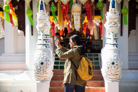 Travelers thai women people travel visit respect praying and use smart mobile phone take photo ancient ruins building shrine of Wat Pa Dara Phirom Temple at Mae Rim city in Chiang Mai, Thailandの写真素材