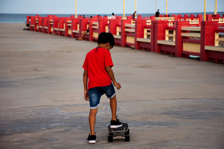 Thai people and foreign travelers travel visit rest relax and exercise playing sport skateboard on street of Saphan saranwithi red bridge at Prachuap bay beach in Prachuap Khiri Khan, Thailandの写真素材