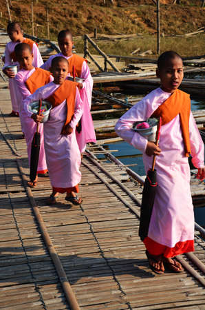 Tradition of almsgiving Burmese nuns women group procession walk on bridge for thai people respect praying put food offerings in morning at Sangkhla Buri on February 2, 2014 in Kanchanaburi, Thailandのeditorial素材