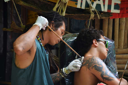 Thai man tattoo artist people write drawing tattoo on back of foreign travelers men travel visit rest relax at local tattoo shop at Ao Nang Railay bay island on April 23, 2011 in Krabi, Thailandのeditorial素材