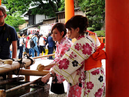 Japanese wear traditional clothing kimono and yukata washing hand rite or mitarashi ritual with chozusha or holy water in wash hand stone basin at Fushimi Inari Shrine on July 11, 2015 in Kyoto, Japanのeditorial素材