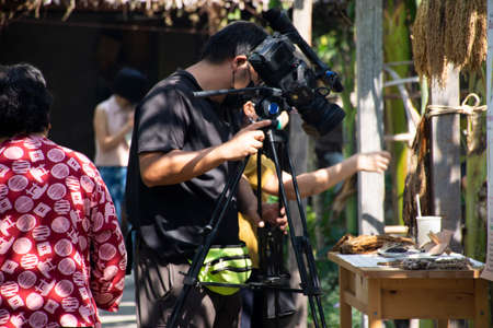 Thai men people reporter use digital camcorder video for broadcast live report news of organic farmer street market festival event fair at garden park outdoor on January 15, 2022 in Bangkok, Thailandのeditorial素材