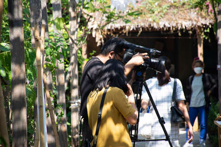 Thai men people reporter use digital camcorder video for broadcast live report news of organic farmer street market festival event fair in garden park outdoor at Nonthaburi city in Bangkok, Thailandのeditorial素材