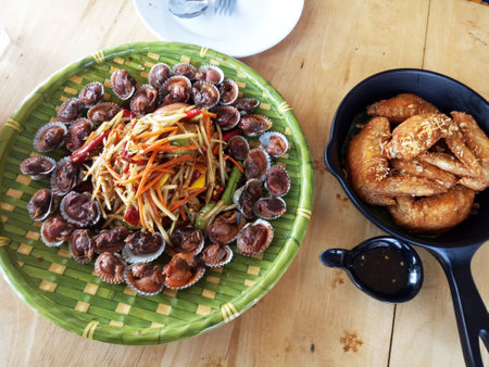 Traditional north east thai food fusion set or local isan cuisine meal somtam with boiled roughly cockle and fried chicken wing serve for people eat drink at restaurant cafe shop in Bangkok, Thailandの写真素材