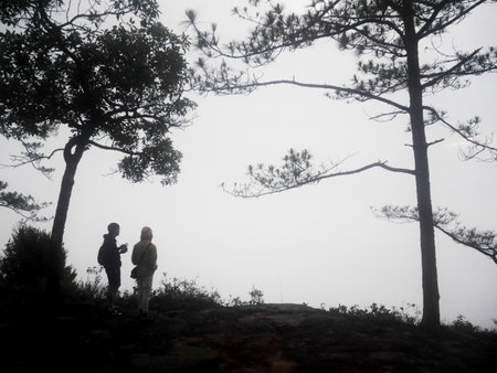 Travelers thai people couple lovers wear raincoat travel visit in forest jungle and camping top mountain for travel while raining mist fog winter season at Phu Kradueng National Park in Loei, Thailandの写真素材