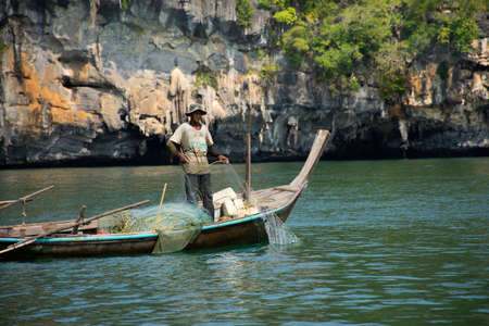 Thai man fisher people sailing wood long tail boat fishery floating in sea use net catch fishing marine and fish in ocean at Mu Ko Petra National Park at Pak Bara on April 12, 2022 in Satun, Thailandのeditorial素材