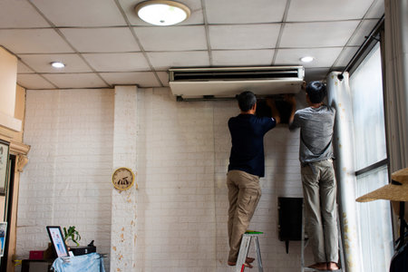 Thai mechanic and air conditioner technician professional working repair and maintenance check availability prepare fix air condition on ceiling at house home on April 16, 2023 in Nonthaburi, Thailandのeditorial素材