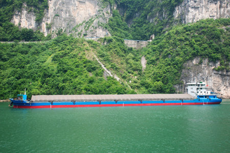 Chinese people drive sail barge and tugboat cargo ship delivery shipping in yangtze river with range mountain cliff of three gorges in Chang Jiang canal in Xiling gorge at Yichang city in Hubei, Chinaの写真素材