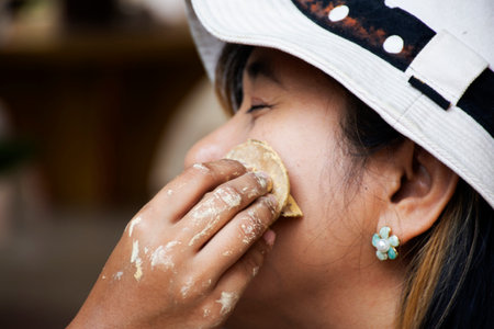 Local Thai Mon children girl using wooden stamp thanaka powder makeup on cheek of women traveler people travel visit join event tribe mon annual celebration at Wat makham temple in Ratchaburi Thailandの写真素材