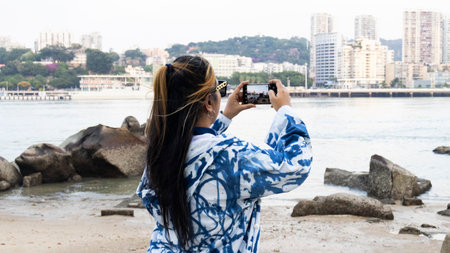 Travelers thai women people wearing indigo clothes travel visit and use smart phone take photo viewpoint stone beach of Lujiang river at Gulangyu Island Town of Pianos at Xiamen city in Fujian, Chinaの写真素材