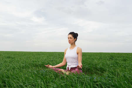 Young slim girl doing yoga outdoors in a green fieldの写真素材