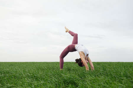 Young slim girl doing yoga outdoors in a green fieldの写真素材