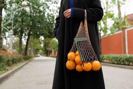 A girl holds a string bag with oranges and a notebook standing on the streetの写真素材