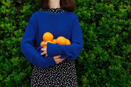 A girl in a blue sweater holds ripe oranges in her handsの写真素材