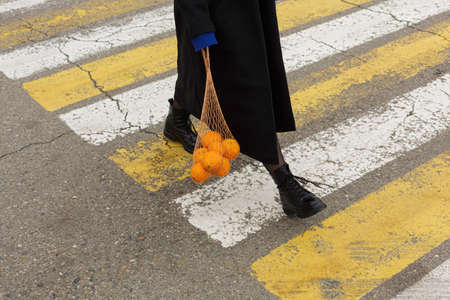 A girl holds a string bag with oranges at a pedestrian crossing