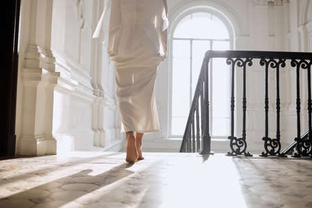 A girl in a wedding dress walks barefoot in a bright hallの写真素材
