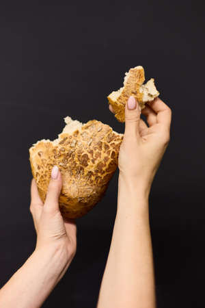 Womens hands break off a piece of fresh bread, close up