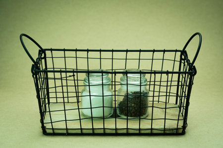 Salt glass jar with spices in metal wire basket on green background.の写真素材