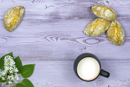 Black mug with milk. Homemade sweet cookies. Sprig and white lilac flowers on the table.の写真素材