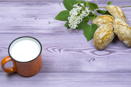 Orange mug with milk. Homemade sweet cookies. Sprig and white lilac flowers on the table. Springの写真素材