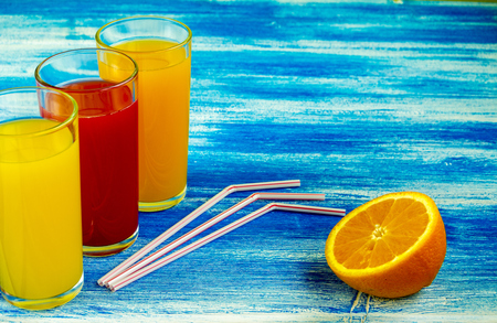 Three glasses of soft drinks are on a blue background. Slices of an orange. Summer drinksの写真素材