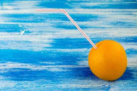 Ripe orange with tube for cocktail on the blue background. Summer drinksの写真素材