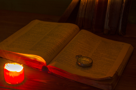 The old book in the library by candlelight. The Bible is on the table. Old pocket watch. Middle Ages. Divination. Prediction. Religionの写真素材