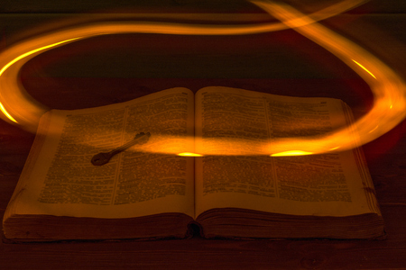 The open Holy Bible is on the table. Ancient key. A fire flying over the Bible illuminates its pages. Religionの写真素材