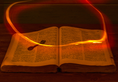 The open Holy Bible is on the table. Ancient key. A fire flying over the Bible illuminates its pages. Religionの写真素材