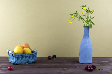 Apricots are in a wicker basket. Cherries are on a wooden table. Vase with wildflowers on a beige background.の写真素材