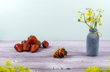Vase with wildflowers. Some strawberry is on the table.の写真素材