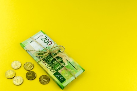 A bundle of money. Russian cash and a few coins. A bundle tied with a rope. Denominations in 200 rubles. On a yellow backgroundの写真素材