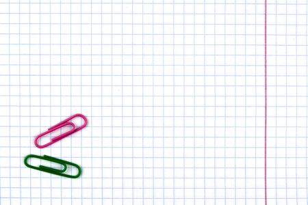Student notebook in a cage with a red line. On the white sheet is two paper clips green and purpleの写真素材