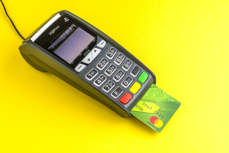 Moscow, Russia, 13.11.2018. Credit card payment terminal on yellow background. Green Plastic card Mastercard inserted into the terminalのeditorial素材