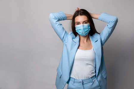 Fashion portrait of young woman wearing a face mask, in a blue suit, isolated on gray background.