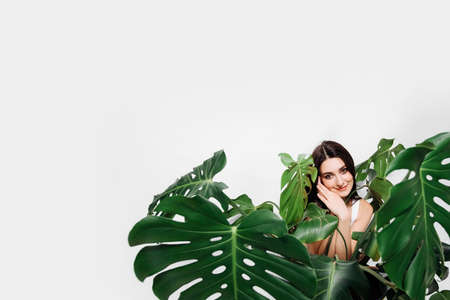 A young girl is sitting in a big green flower of a monstera. She smiles sweetly. She has dark hair. Isolated on white backgroundの写真素材