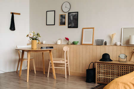 Wooden dining table in a bright home interior. On the table are peonies in a designer yellow vase ....