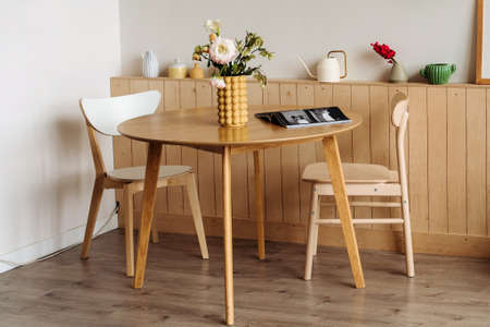 Wooden dining table in a bright home interior. On the table are peonies in a designer yellow vase .の写真素材