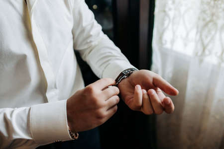 A sexy male businessman fastens a cufflink on his wrist watch, the cuff of the sleeve of a luxurious...
