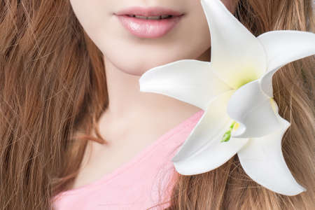 Portrait of a beautiful young girl with a Lily flower in her hair. Close-up portrait. Lips in the frame . Beautiful pink lips.The concept of hair care. lips with lip gloss. A lipstick kiss.の写真素材